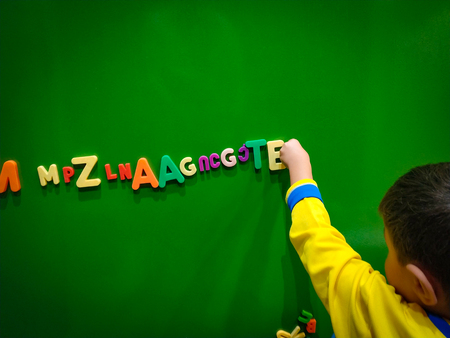 Little boy playing magnetic letters on a green boardの写真素材