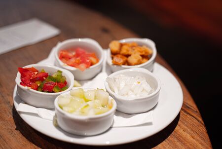 Different bowls with small pieces of fresh tomato, onion, pepper, cucumbers and some croutonsの写真素材
