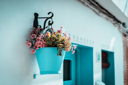 Pink flowers in a blue bucket hung on a white wall, typical mediterranean villageの写真素材