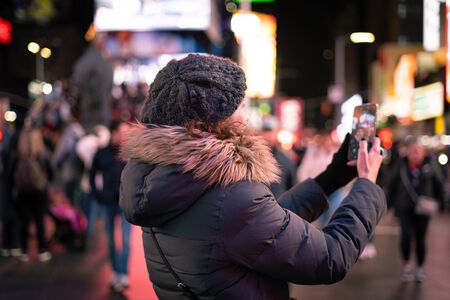Beautiful curly brunette woman taking a selfie with her smartphone in Times Square, New york City.の写真素材