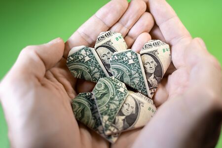 Hands holding one Dollar origami hearts on a green backgroundの写真素材