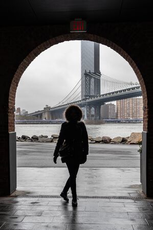Silhouette of a tourist woman with warm clothes with the Manhattan Bridgeの写真素材