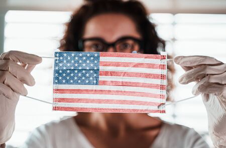 Pandemic Coronavirus. Close up of young woman with surgical mask with the USA flag on itの写真素材