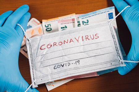 Hand with euro bills covering a face mask with the word coronavirusの写真素材