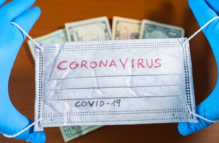 Hand with a face mask with the word coronavirus covering dollar billsの写真素材