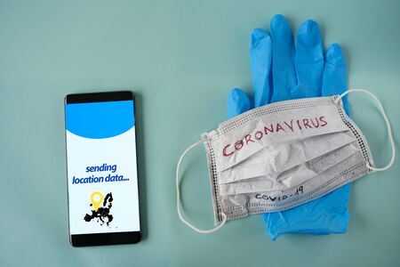 White medical mask, blue globe and Phone with location surveillance software on screen isolated on cyan backgroundの写真素材