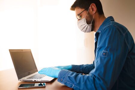 Man with face mask and blue gloves working from home and worried about covid-19 coronavirusの写真素材