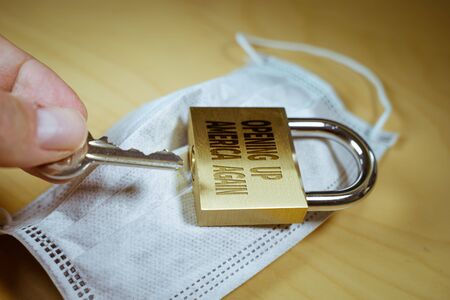 Hand opening a padlock with the Opening up america again text on it.