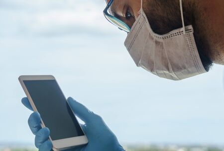 Extreme close-up portrait of a man wearing surgical mask and looking at the smartphoneの写真素材