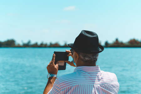 Senior man tourist taking a photo with his smartphone and wearing disposable face mask.の写真素材