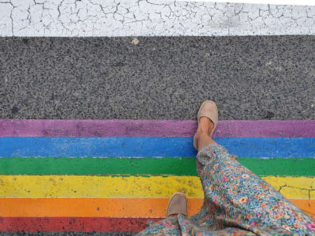woman crossing a pedestrian crossing with the colors of the LGTBI flag.の写真素材