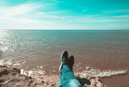 First person perspective shot from a hiker sitting at the edge of a cliff over blue seaの写真素材