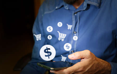 Man using a smartphone with US dollar and shopping cart icons.の写真素材