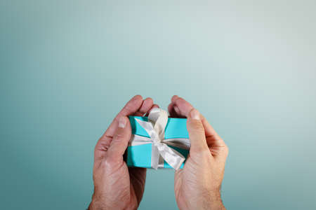 hands holding a turquoise gift boxe tied with white silk ribbonの写真素材