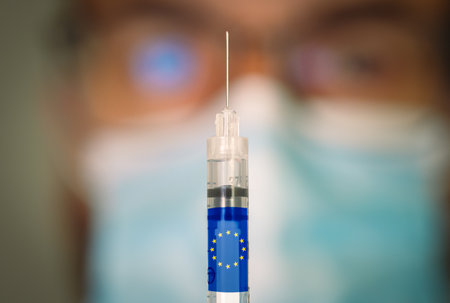 Close-up of hypodermic syringe with the EU flag and blurred doctor on the background.の写真素材