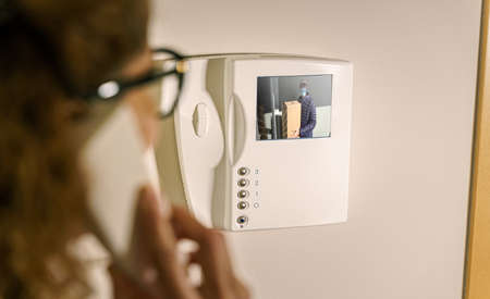 delivery man wearing a protective mask talking on the intercom with a woman to deliver a package.の写真素材