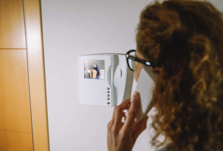 delivery man wearing a protective mask talking on the intercom with a woman to deliver a package.の写真素材