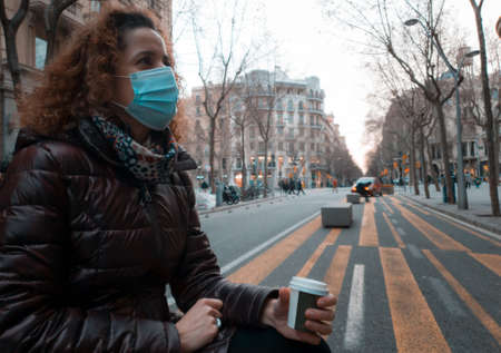 woman with a mask having a takeaway coffee in a street in barcelonaの写真素材