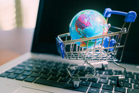 Small shopping cart with world globe in it over a laptop.の写真素材