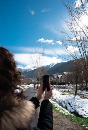 Beautiful curly brunette woman taking selfie self-portrait on snow mountainの写真素材