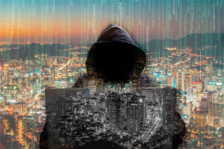 silhouette of a man in a hood working as a hacker at the computer in the dark room at night, hacking the system and laundring secret information.の写真素材