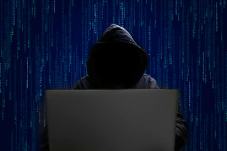 silhouette of a man in a hood working as a hacker at the computer in the dark room at night, hacking...