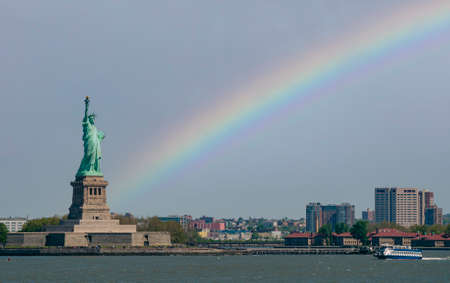 Statue of liberty in new york city and a rainbow in the sky on the backgroundの写真素材