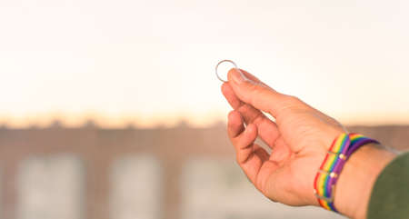 close-up view of a mans hand showing a ring with an LGBT rainbow wristband.