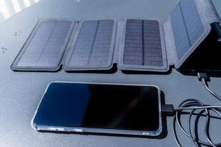 Charging a smartphone from home with a portable solar panel charger.の写真素材