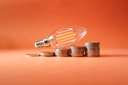 led light bulb on top of coins in the form of an ascending graph, symbolizing the rising cost of electricity.の写真素材