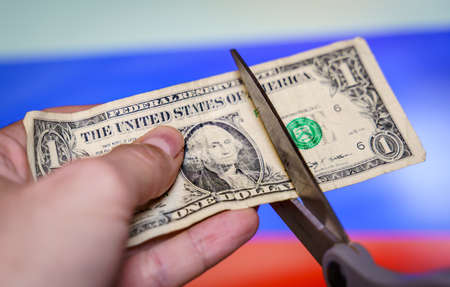 hand with scissors cutting a dollar bill with the russian flag in the background.の写真素材