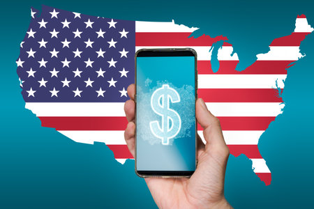 Hand holding a smartphone with a digital US Dollar on screen with the map of USA in the backgroundの写真素材