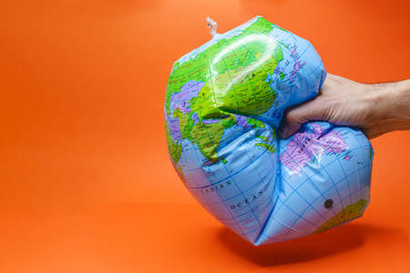 Hand tightly gripping an earth globe on orange background.の写真素材