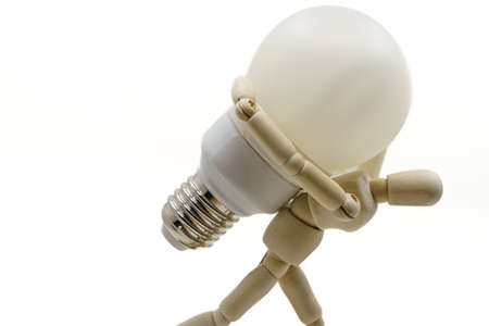 wooden doll holding a light bulb on his shoulders . Concept of rising electricity pricesの写真素材