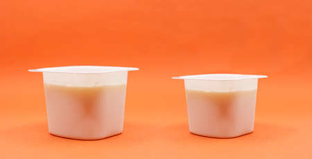 reduced yogurt on an orange background. Inflation, skimpflation or shrinkflation concept of less for the same price.の写真素材