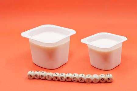 Reduced yogurt on an orange background. Inflation, skimpflation or shrinkflation concept of less for the same price.の写真素材