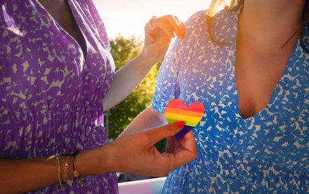 Anonymous lesbian couple sharing a heart with the colors of the rainbowの写真素材