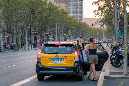 tourist taking a yellow and black typical barcelona taxi in passeig de gracia street in barcelonaのeditorial素材