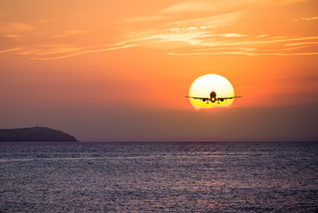Passenger airplane silhouette agaist a sunset over the oceanの写真素材
