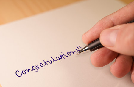 Close-Up of Hand Writing Congratulations with Pen on Paperの写真素材