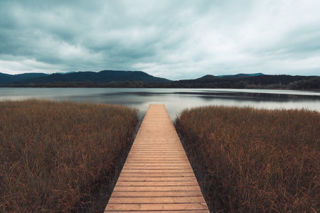 Wooden boardwalk extending into Lago Banyolas on a cloudy autumn dayの写真素材