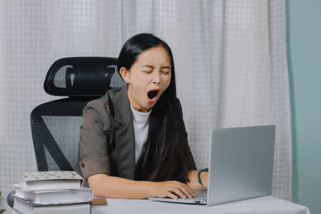 Asian woman yawning while working on laptop in her office.の写真素材