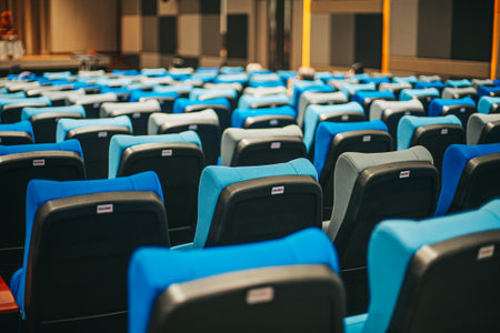 Interior of a conference hall with rows of blue seats and chairs.
