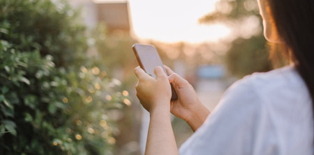 Woman use of mobile smart phone in the park at sunset time.の写真素材