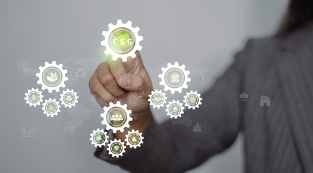 Hand touching ESG icon on virtual screen for environmental, social, and governance in sustainable and ethical business on a green background.の写真素材