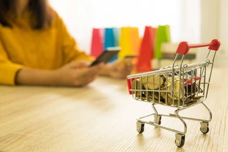 Money in a trolley on table,  background women holding credit card and using mobile Phone buy product . Online shopping conceptの写真素材