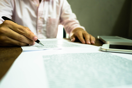 Businessman working at office with laptop and documents on the table, Businessman holding pens and papers taking notes in documents on the table.の写真素材
