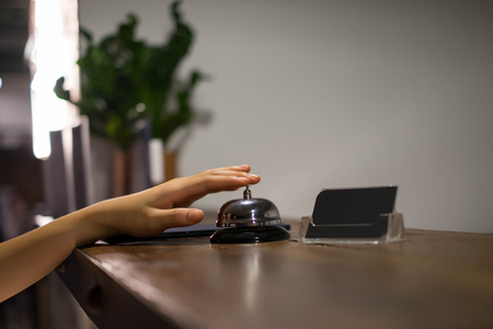 Close up women call hotel reception on counter desk with finger push a bell in lobby hotel. hotel...