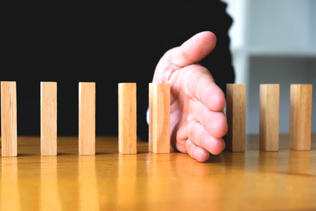 Business hand stops domino continuous overturned meaning that hindered business failure. Stop over this business failure concept.の写真素材