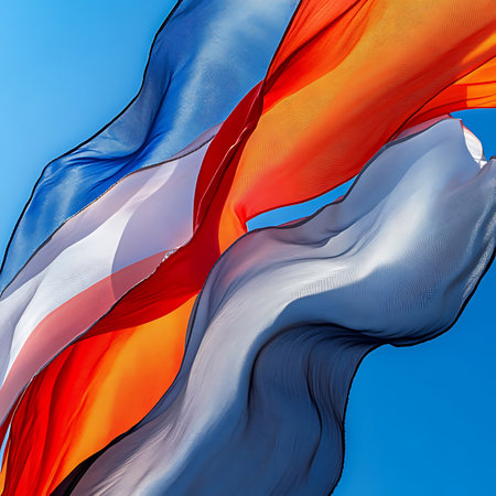 This image showcases vivid flowing fabric in blue, red, and yellow hues, gracefully waving in the breeze under a bright sunny sky, creating a stunning visual effect.の素材